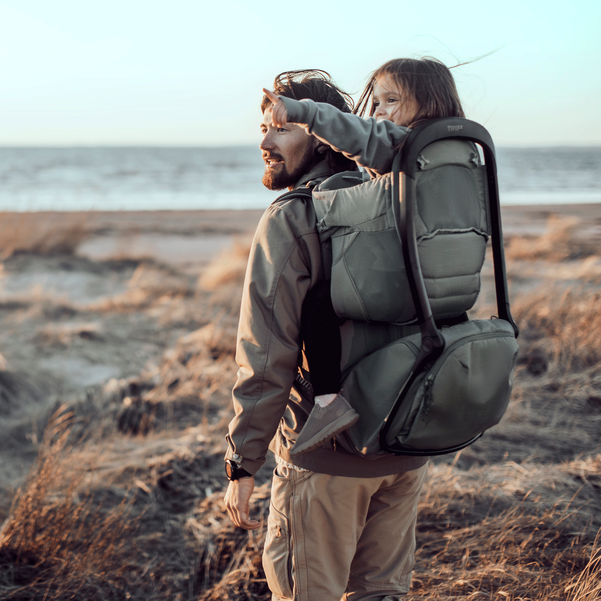 A man goes for a hike by the beach with a child in the Thule Sapling baby hiking backpack.