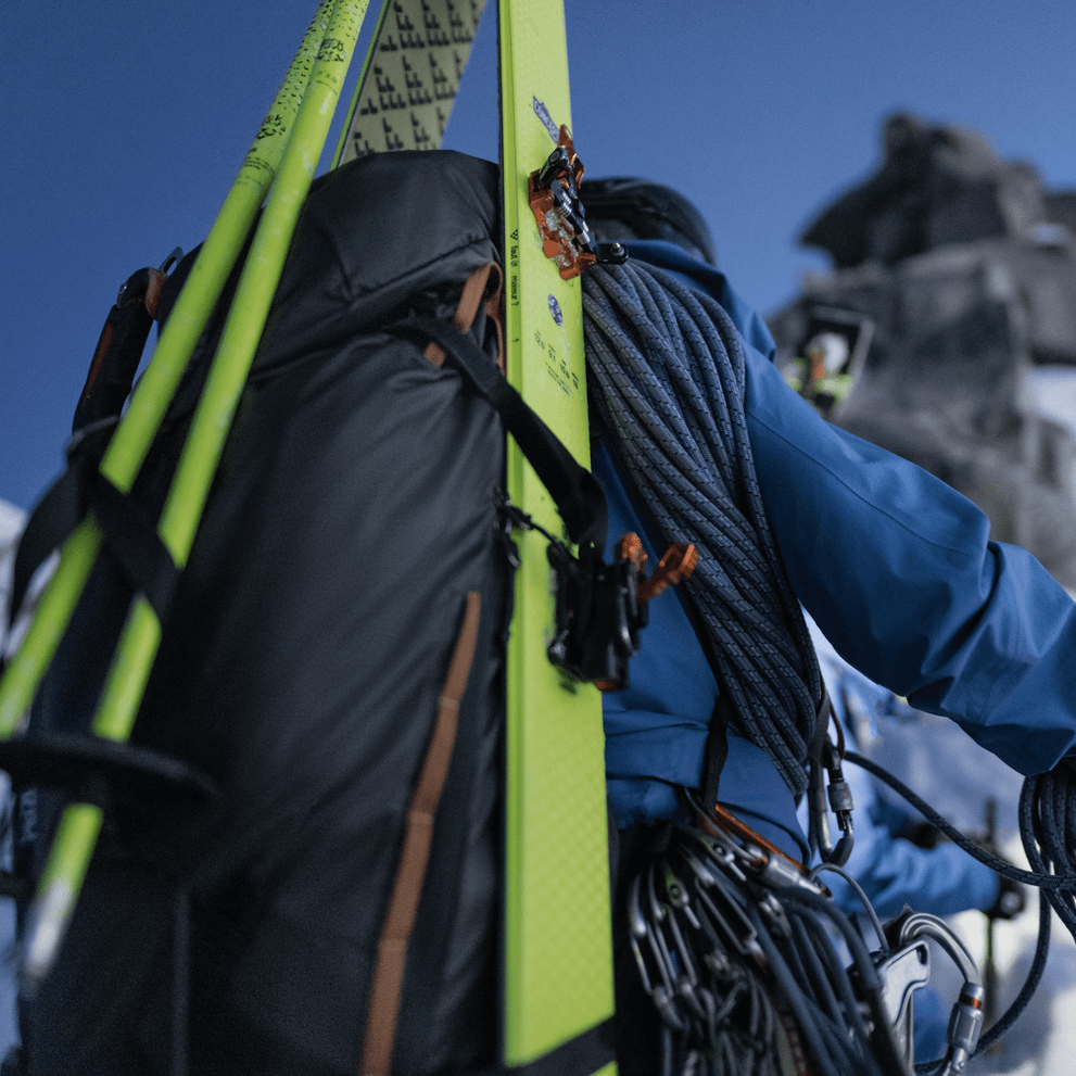 Someone on a snowy mountain carrying skis and rope on their Thule Stir Alpine 40L ski backpack.