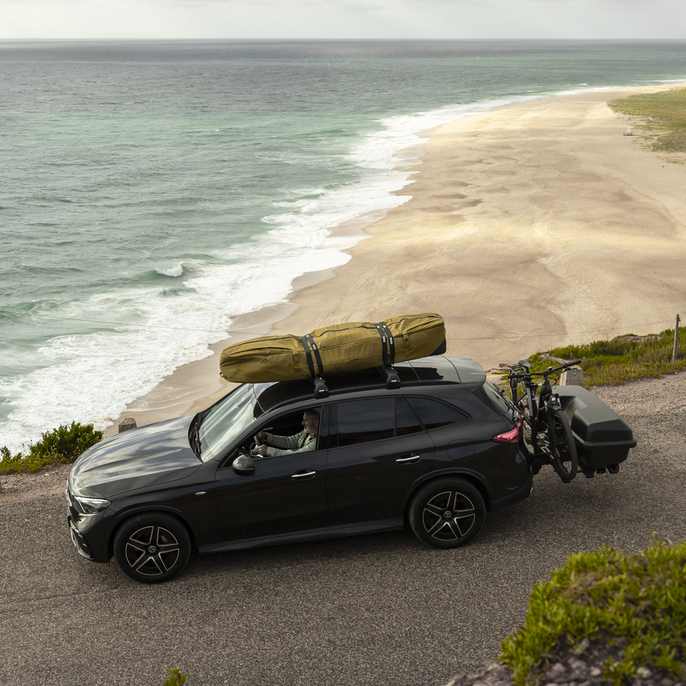 Car parked by the ocean with a Thule Aion surfboard bag mounted on the roof