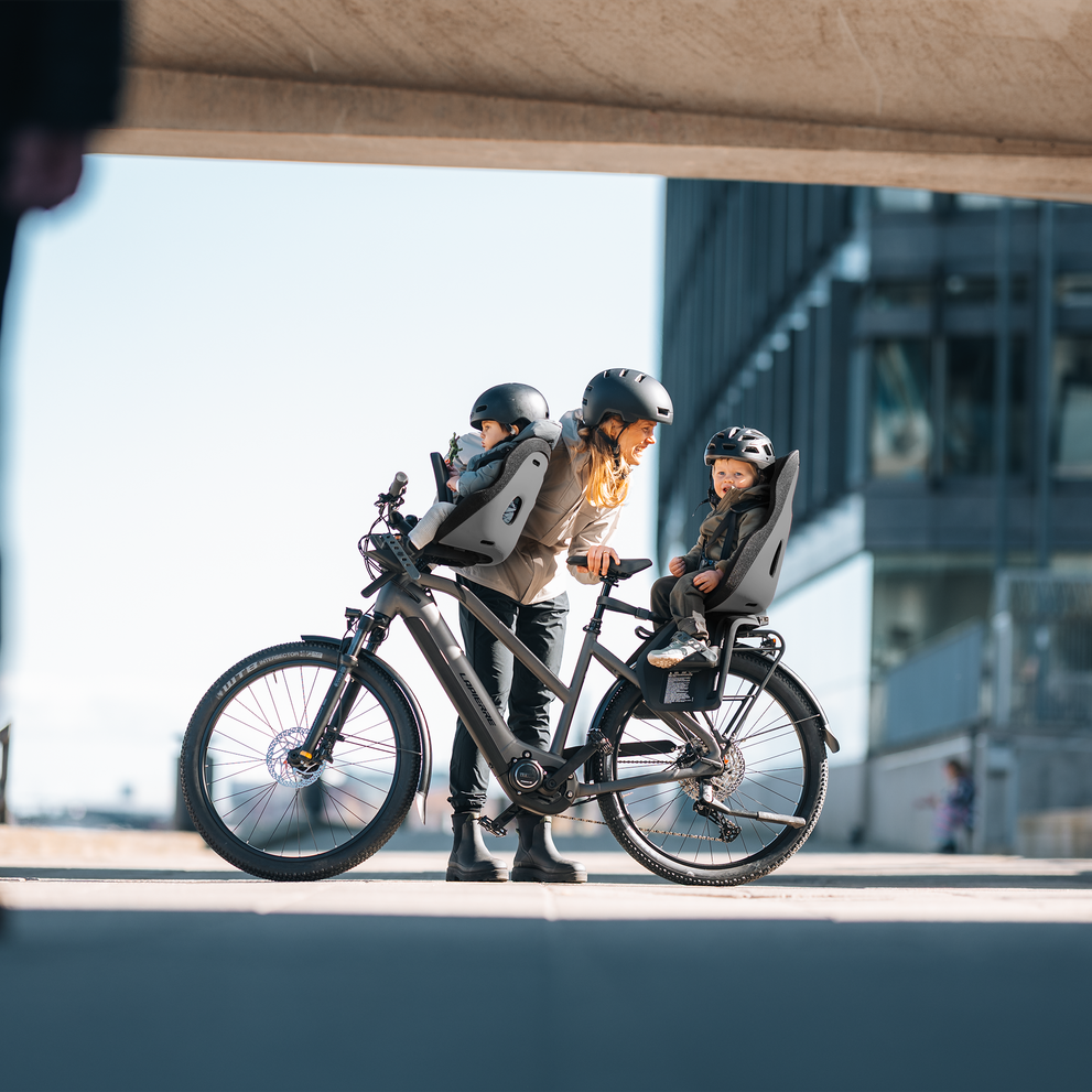 Warm moment with a parent talking to children seated in Thule Yepp Nexxt 2 bike seats, paused beneath a bridge.