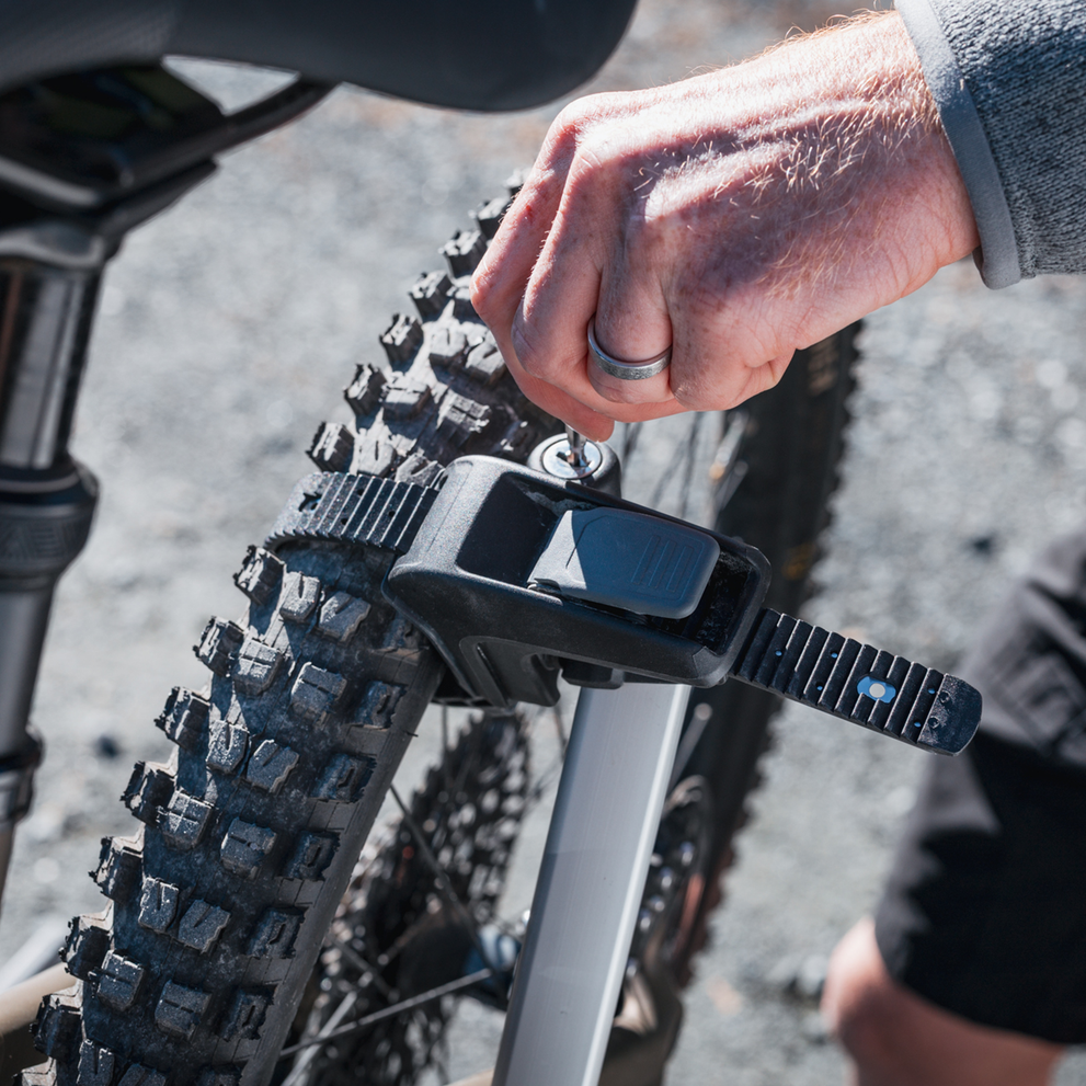 A man is locking one of the pivoting bike arms to a bike wheel on the Thule Vero hitch bike rack.