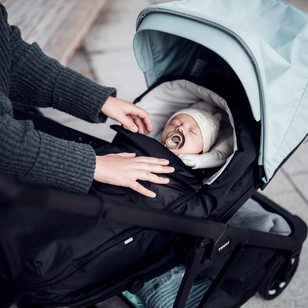 A close-up of a baby bundled and sleeping with a pacifier inside a blue Thule Shine compact baby stroller.