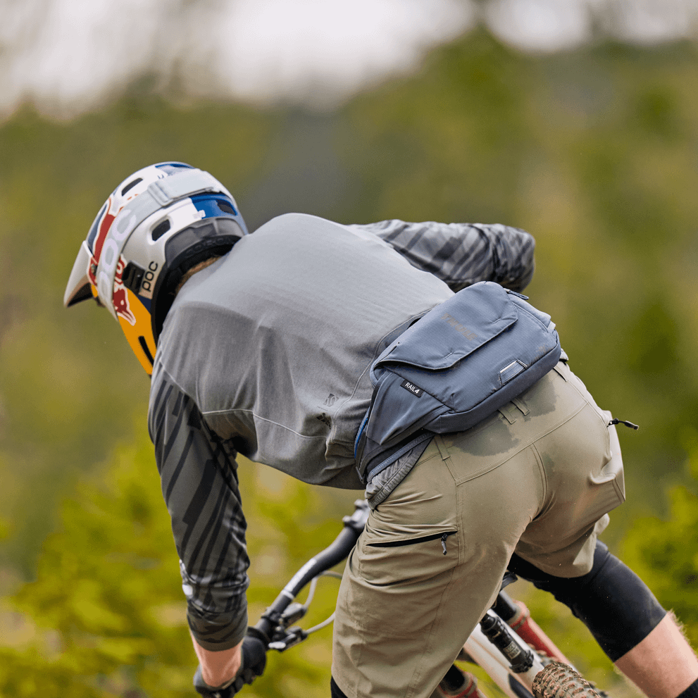 A mountain biker on the trail with a helmet carrying a Thule Rail 4L hydration Hip Pack.
