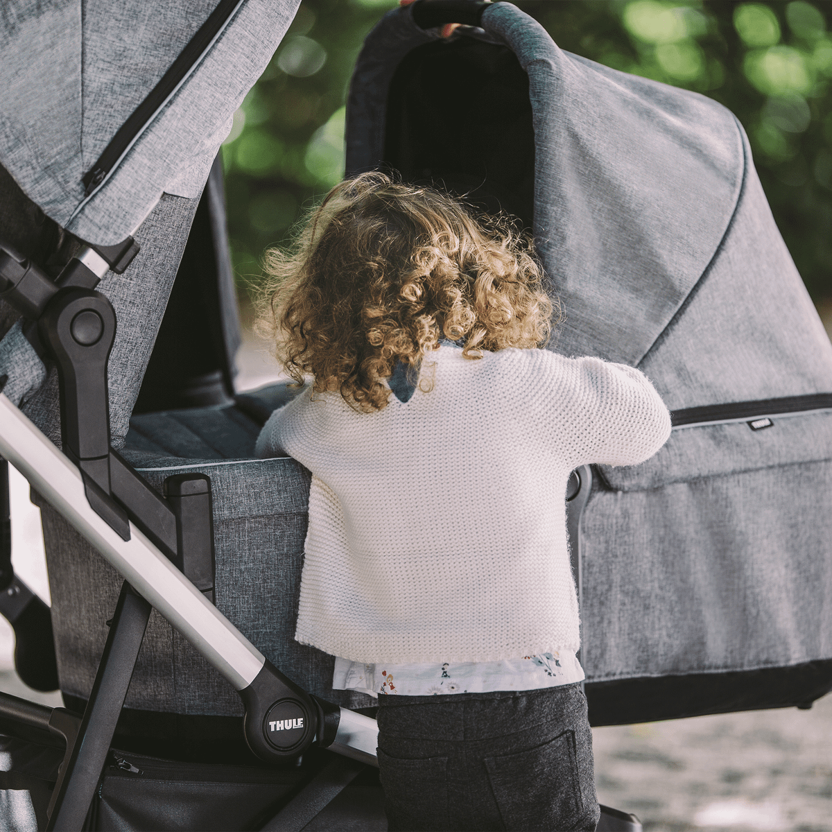 A child peers inside the gray Thule Sleek Bassinet on the Thule Sleek double stroller.