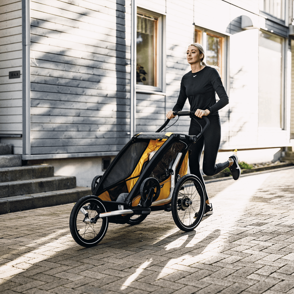 A woman runs down a street pushing her child bike trailer using the Thule Jogging Kit.