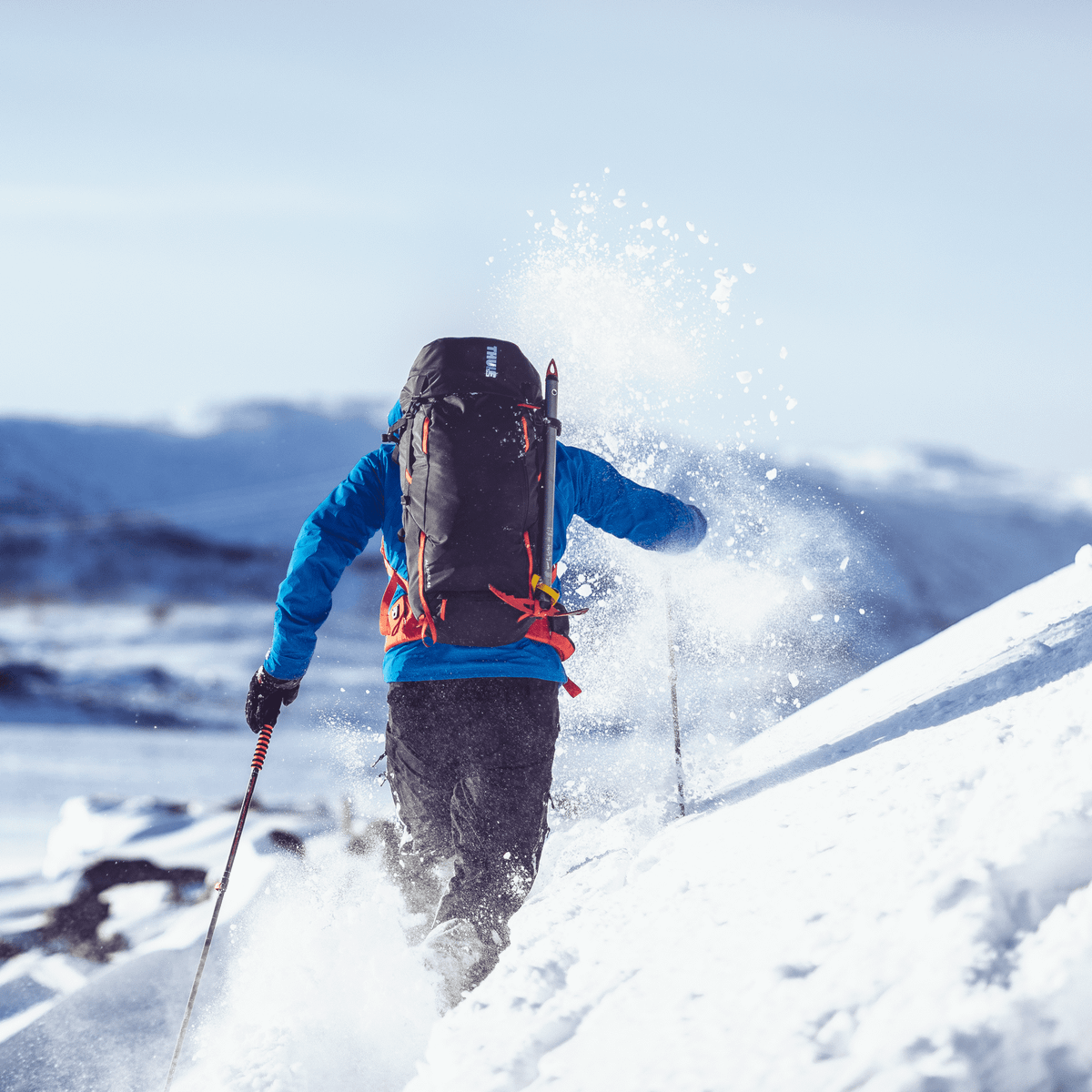 A man cross country skis in the snowy mountains carrying a Thule AllTrail 45L backpack.