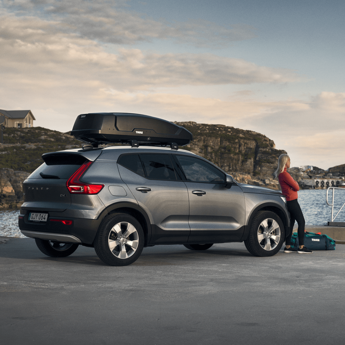 A woman is leaning on a car with a Thule Force XT roof box.