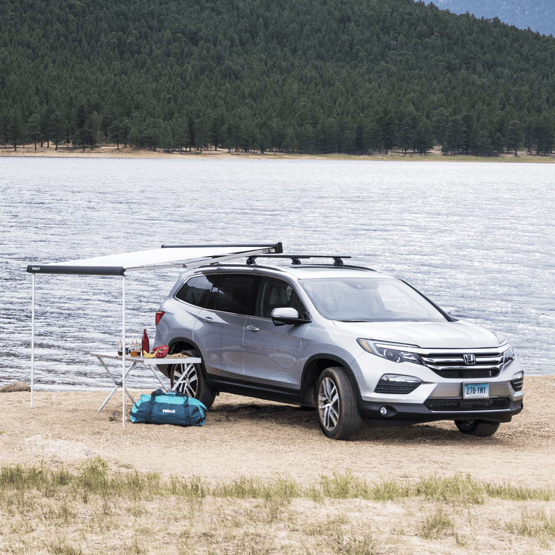 A group of people sitting on a beach close to a car with a Thule Outland Awning