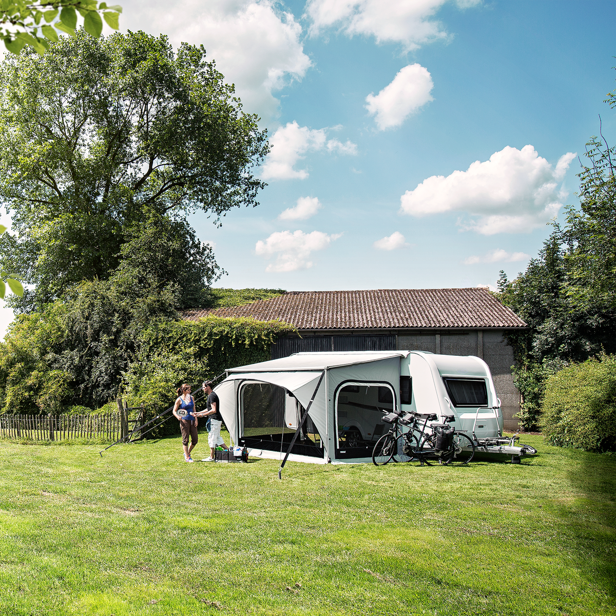 A caravan with a Thule Omnistor 1200 caravan awning and tent are parked in the grass.