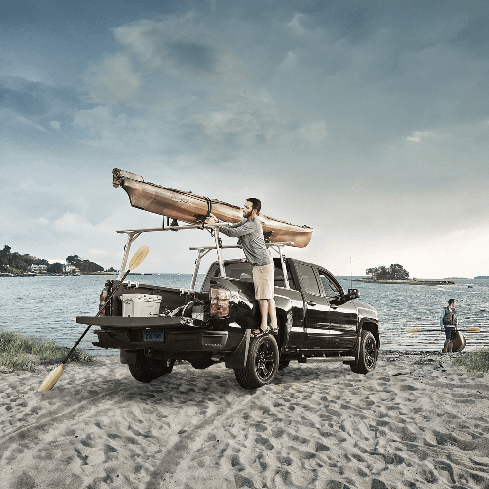 A man is loading a kayak on his pick-up truck on the beach