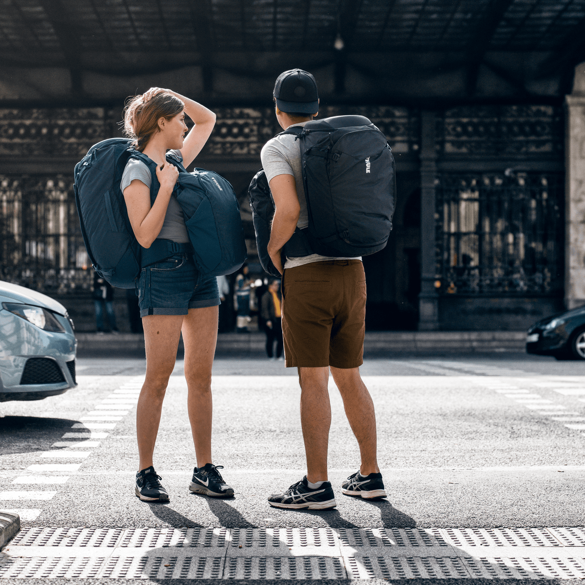 A couple stand on the street outside a train station carrying Thule Landmark 60L backpacking backpacks.