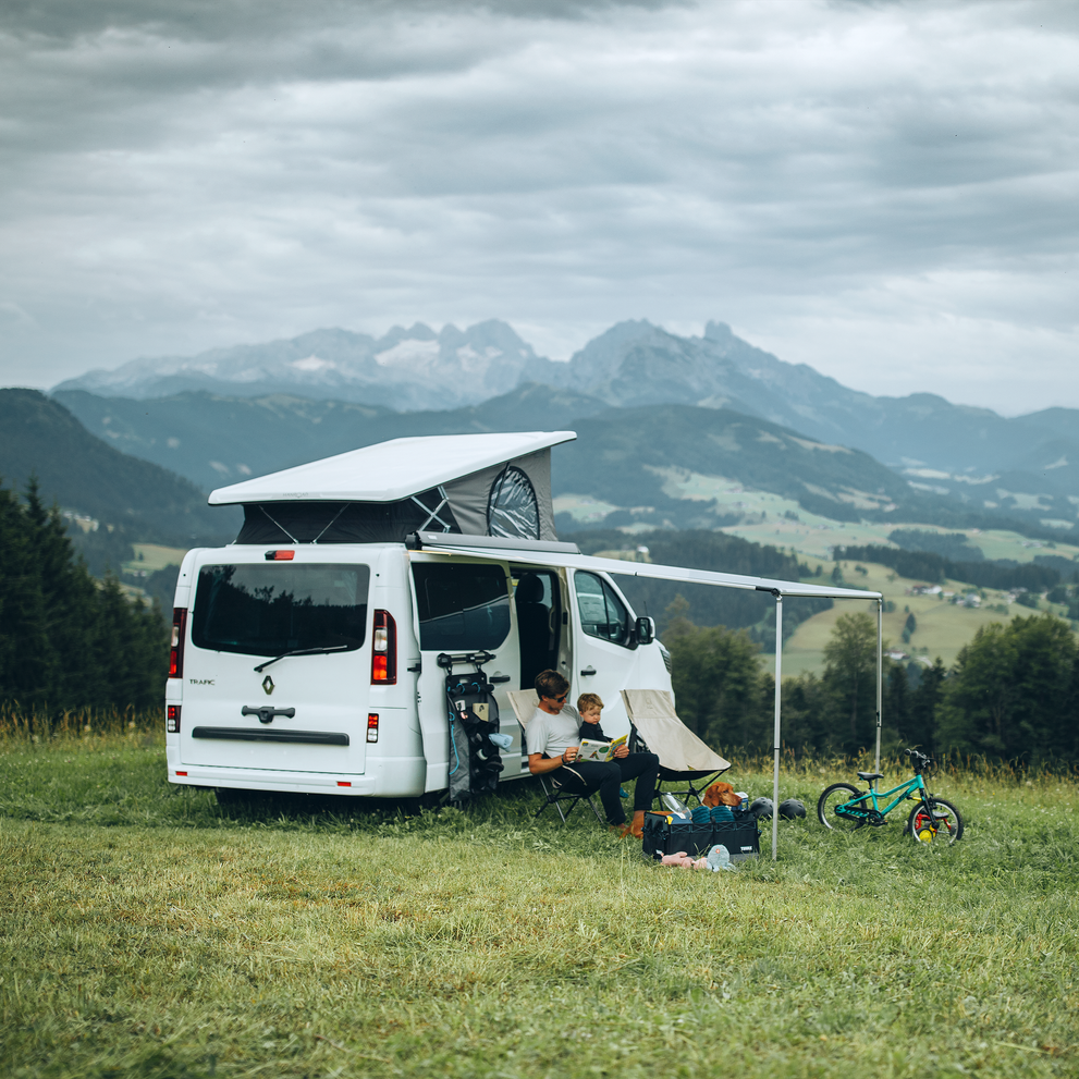 A van with a pop-up roof is parked by the mountain with a Thule 3200 van awning.