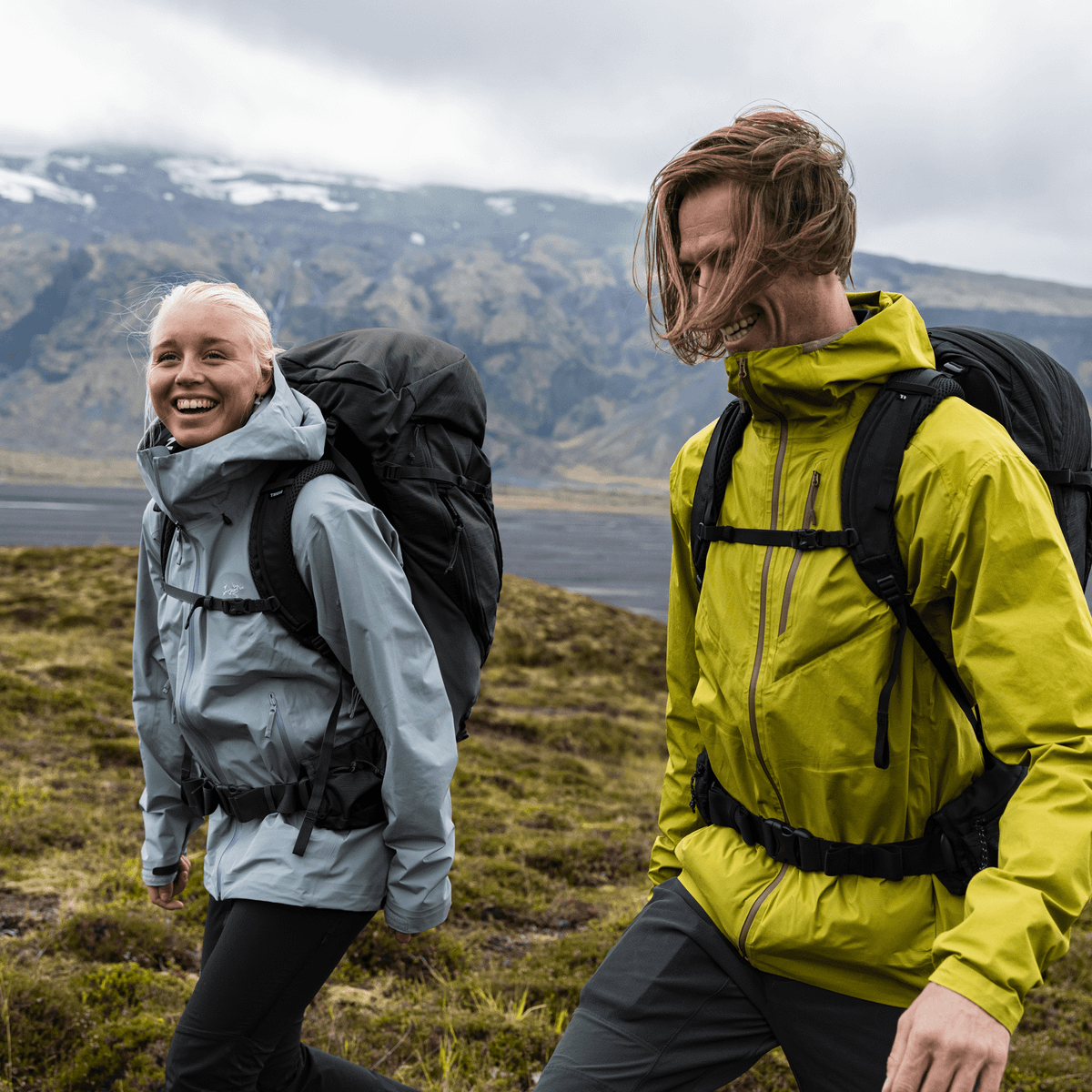 A man and women walk away from a mountain wearing jackets, carrying Thule Topio 40L hiking backpacks.