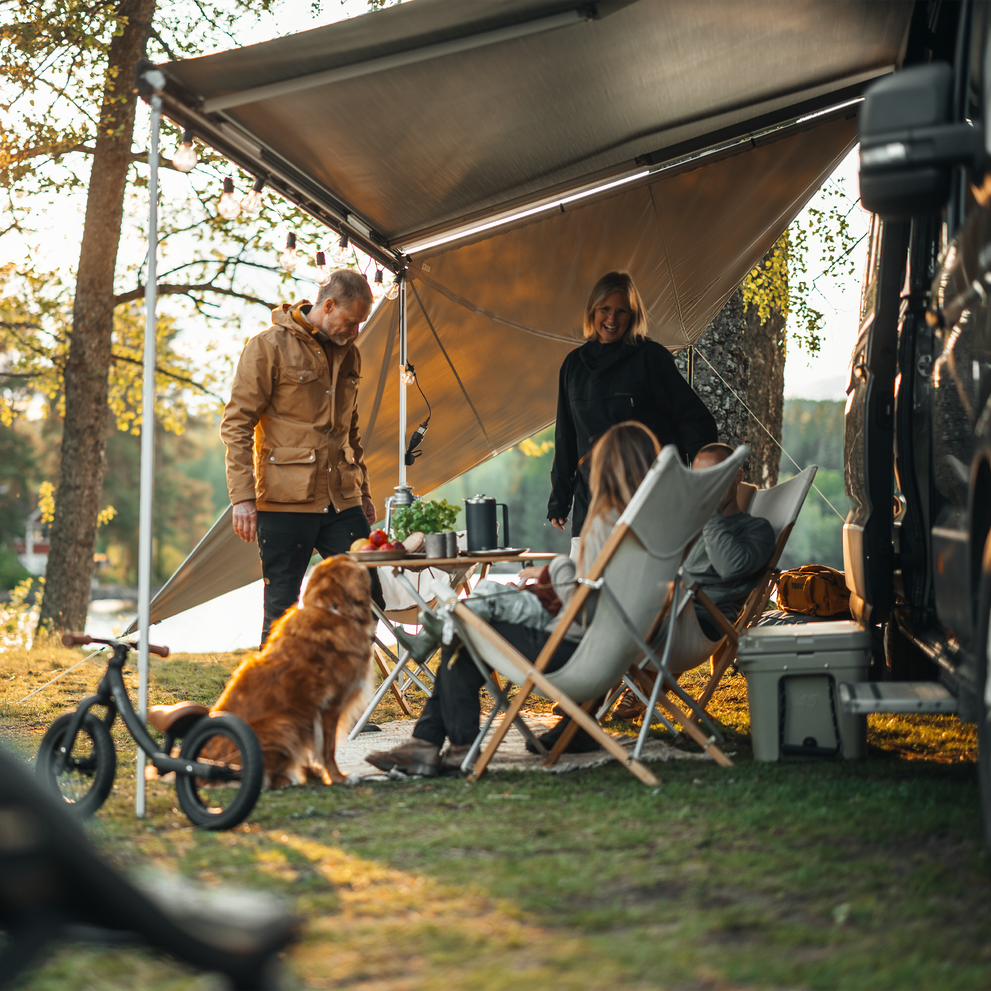 A group of people sitting under an awning with panels gathered around a table.