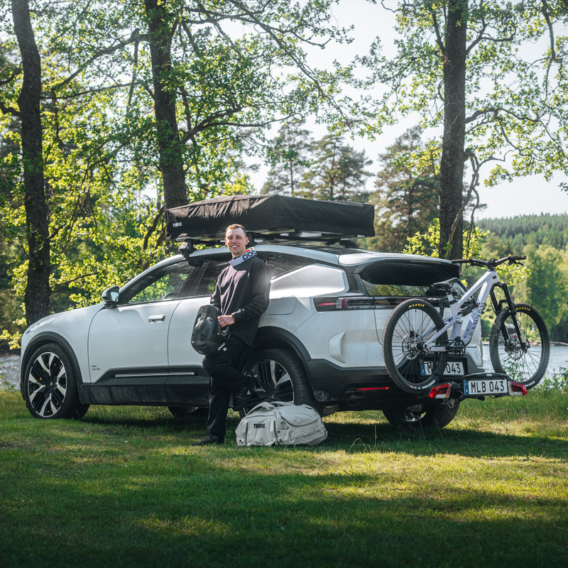 A man is standing beside a car with Thule VeloLite towbar bike carrier mounted on the back of a car, with a bike secured on the bike carrier.