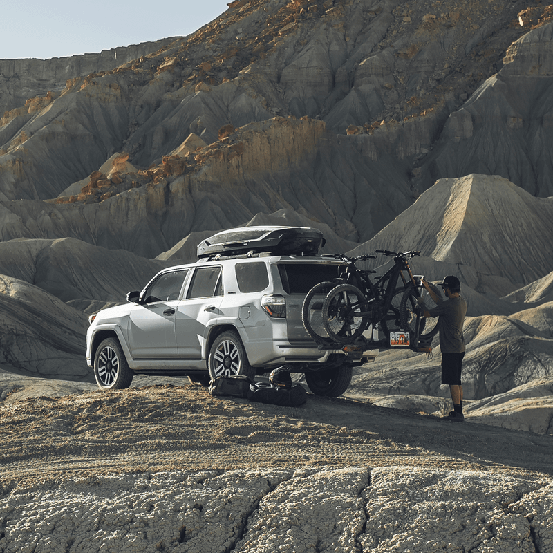 A man loads his bikes into a vehicle with the Thule Verse bike rack parked in the desert.
