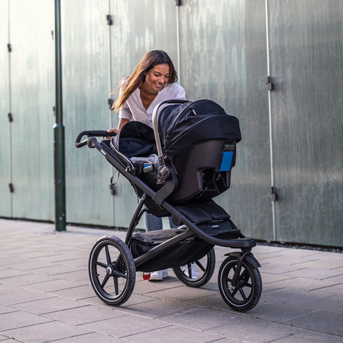 A woman tends to her baby in a black car seat thanks to the Thule Urban Glide 2 Car Seat Adapter.