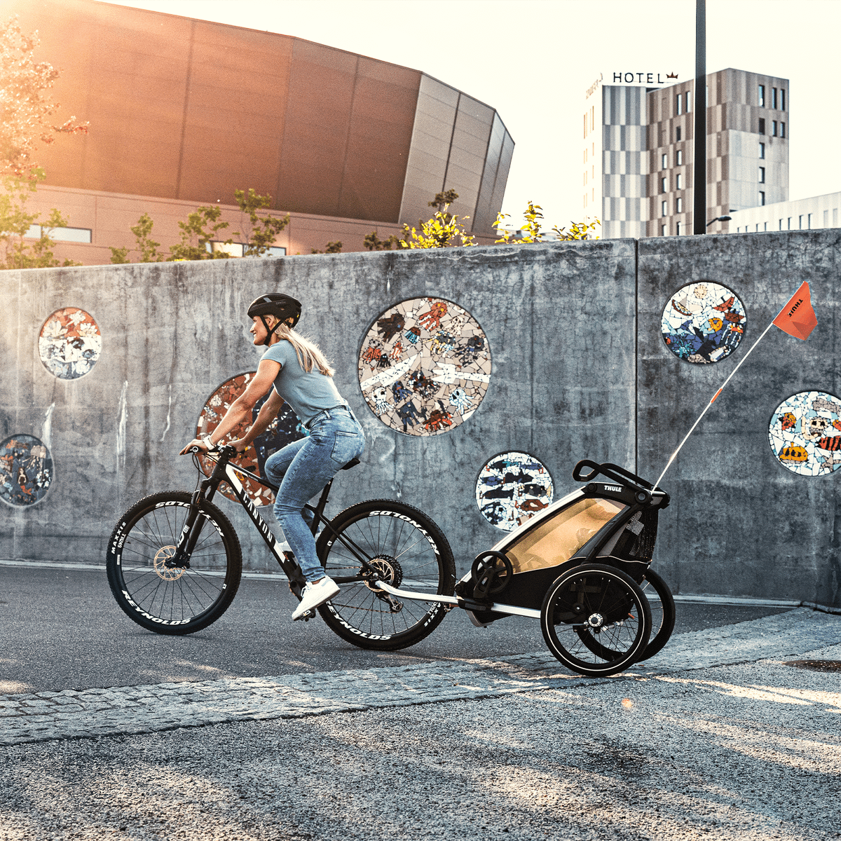 A parent bikes past an artsy wall with a Thule Chariot Lite bike trailer.