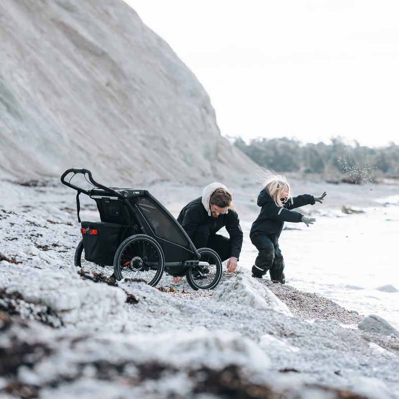 A parent and child by the shore with the Thule Chariot Sport 2, ready for the next family adventure.