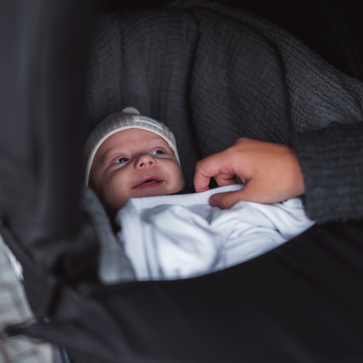 A close-up of a smiling baby inside the bassinet of a Thule Urban Glide 2 all-terrain stroller with bassinet.