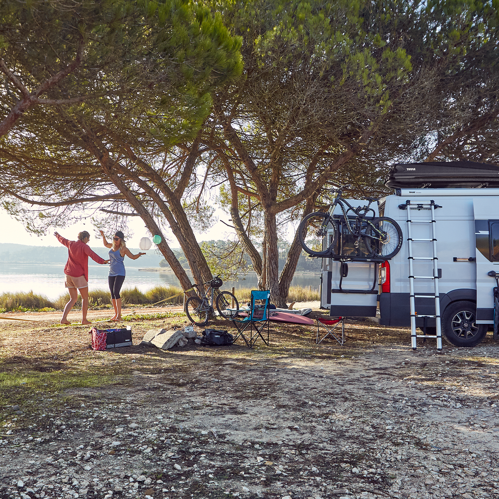 Two people stand by the beach next to an RV with a Thule Elite Van XT bike rack.
