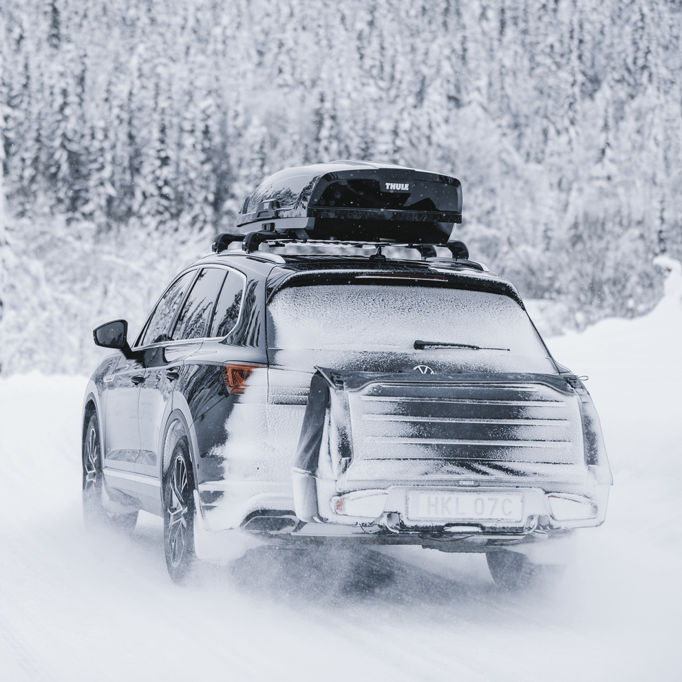 A car with a roof top box and a Thule Onto cargo box driving down the road in a snowy landscape.