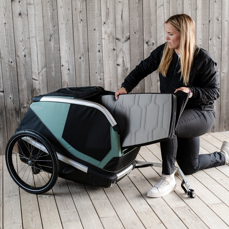 A person kneeling in front of the Thule Bexey dog bike trailer, inserting a light grey cushion.