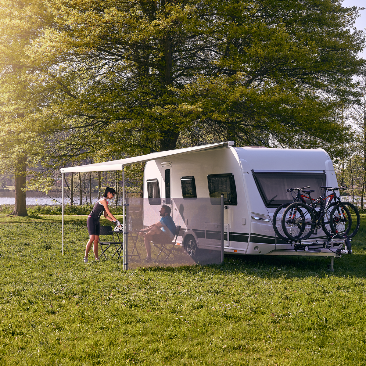 An rv is parked in the grass and a person walks towards the Thule View Blocker Side awning side wall.
