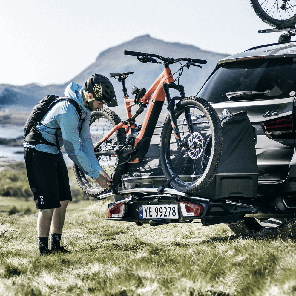 A man is loading bike to a bike carrier mounted on the towbar.