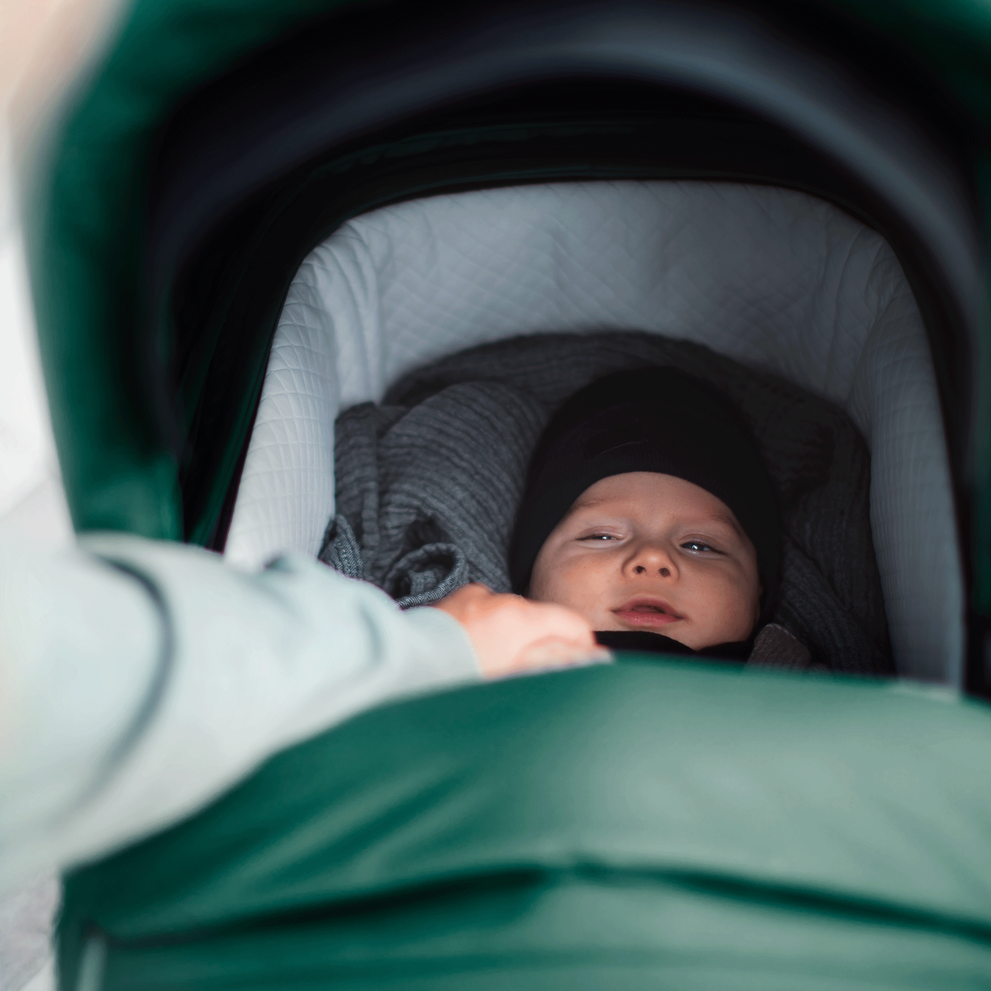 A close-up of a baby inside the green bassinet of a Thule Sleek baby stroller.