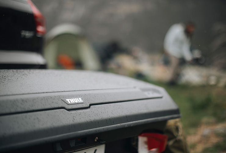 A close up of a Thule Arcos cargo box on a car parked in green nature