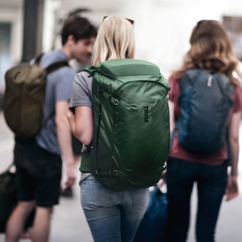 Three friends stand on a train platform carrying Thule Landmark travel backpacks.