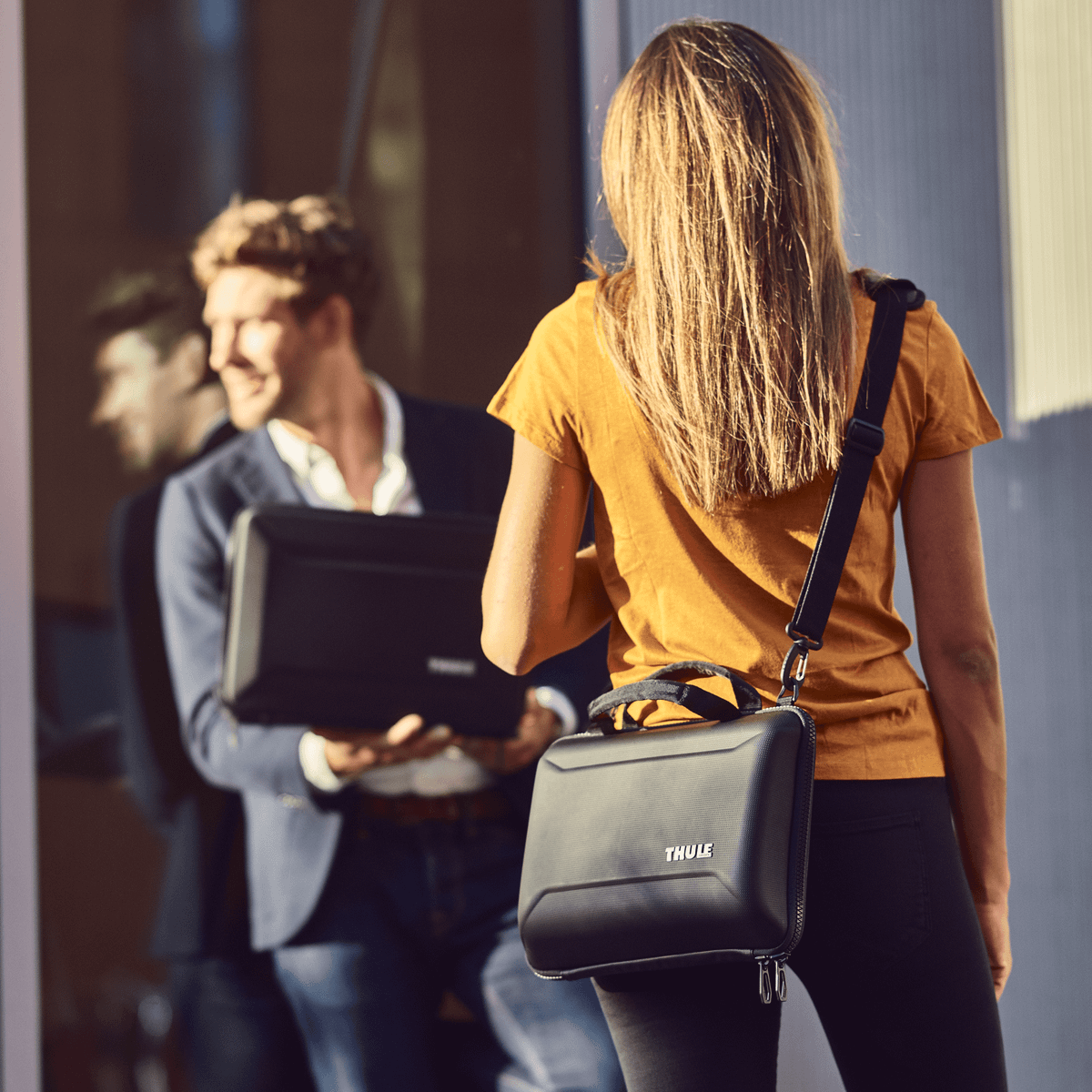 A man and women stand in professional clothing carrying a black Thule Gauntlet 4 MacBook Pro Attaché.