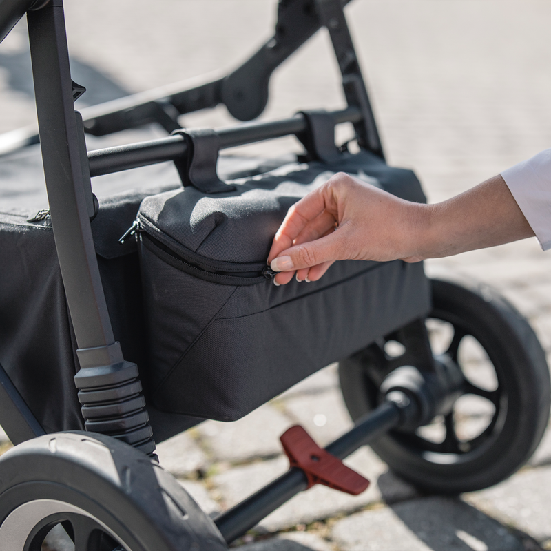 A hand unzips the Thule Stroller Organizer attached to the stroller.