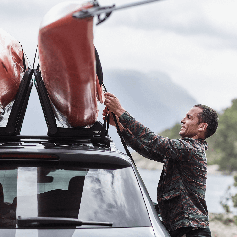 Closeup of a man fastening a kayak on a car roof with a Thule Hull-a-Port Aero