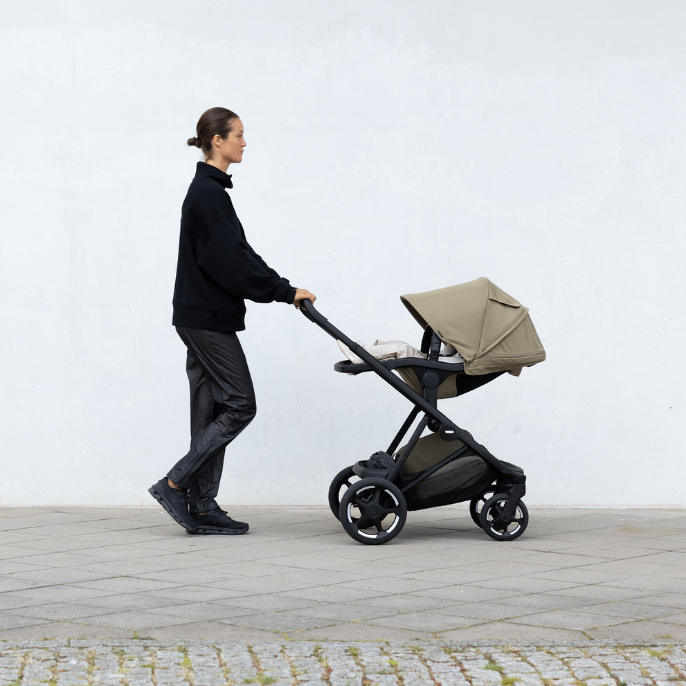 Žena tlačí kočárek Thule Charm v městském prostředí.