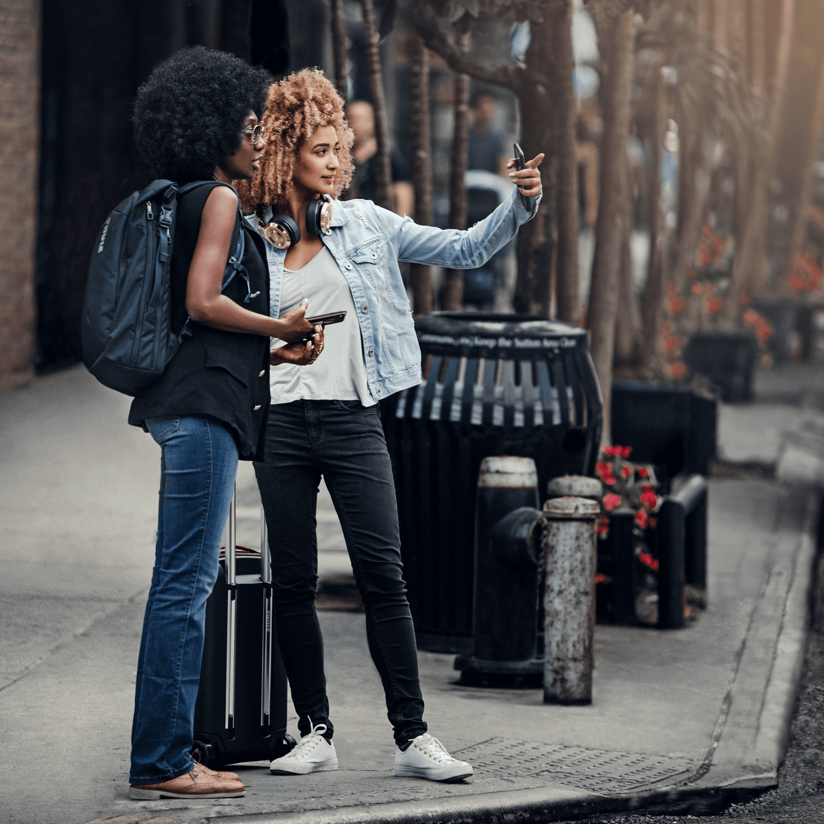Two women look across a busy street with a blue Thule Subterra Travel Backpack.