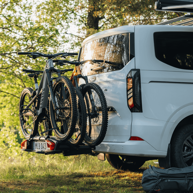 Minivan parked in a scenic setting with Thule VeloSpace 3 towbar bike rack mounted at the rear, carrying three bikes.