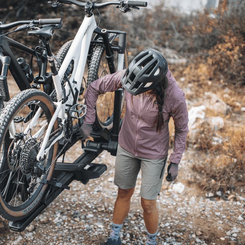 A cyclist loads her bike into the Thule Verse hitch bike rack wearing a helmet.