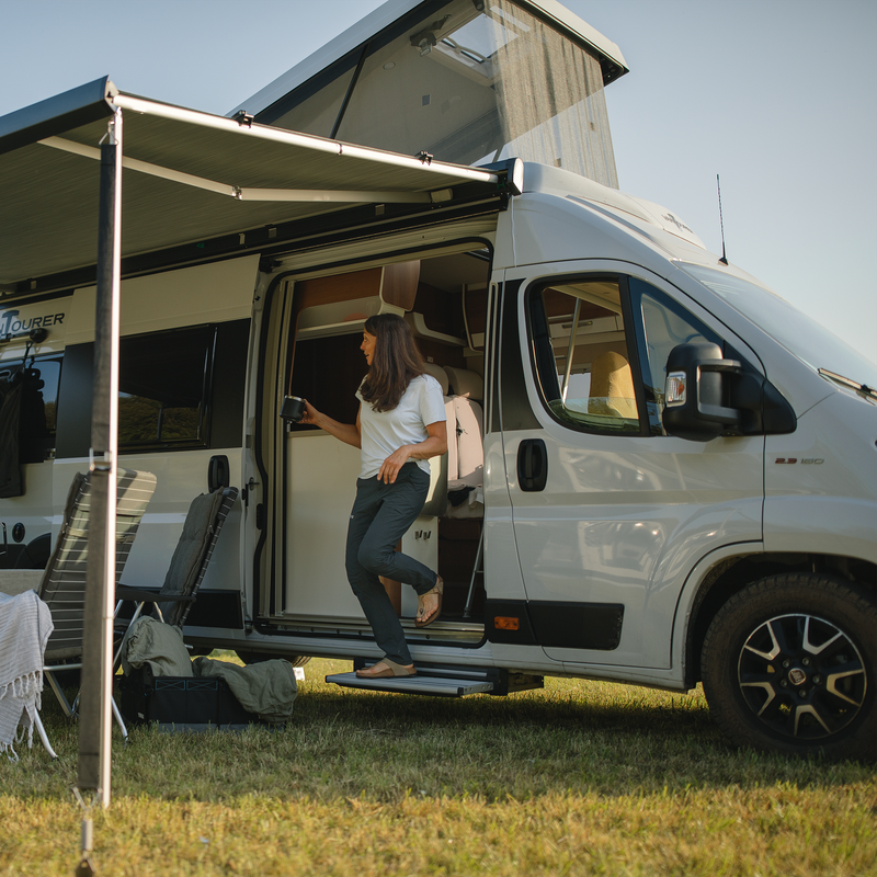 On a van, a woman stands on a Thule Slide-Out Step van step.