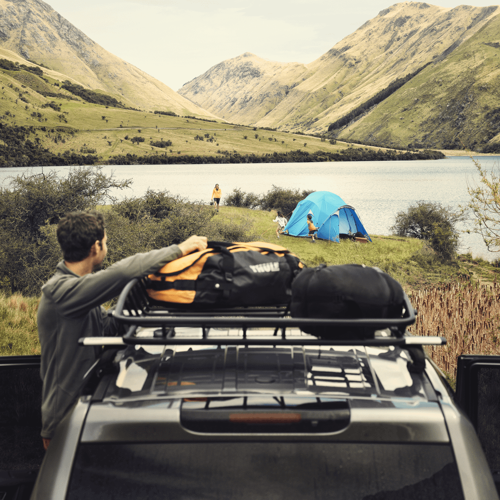 A man unloads his gear from a bag on a roof platform on a car standing by a lake