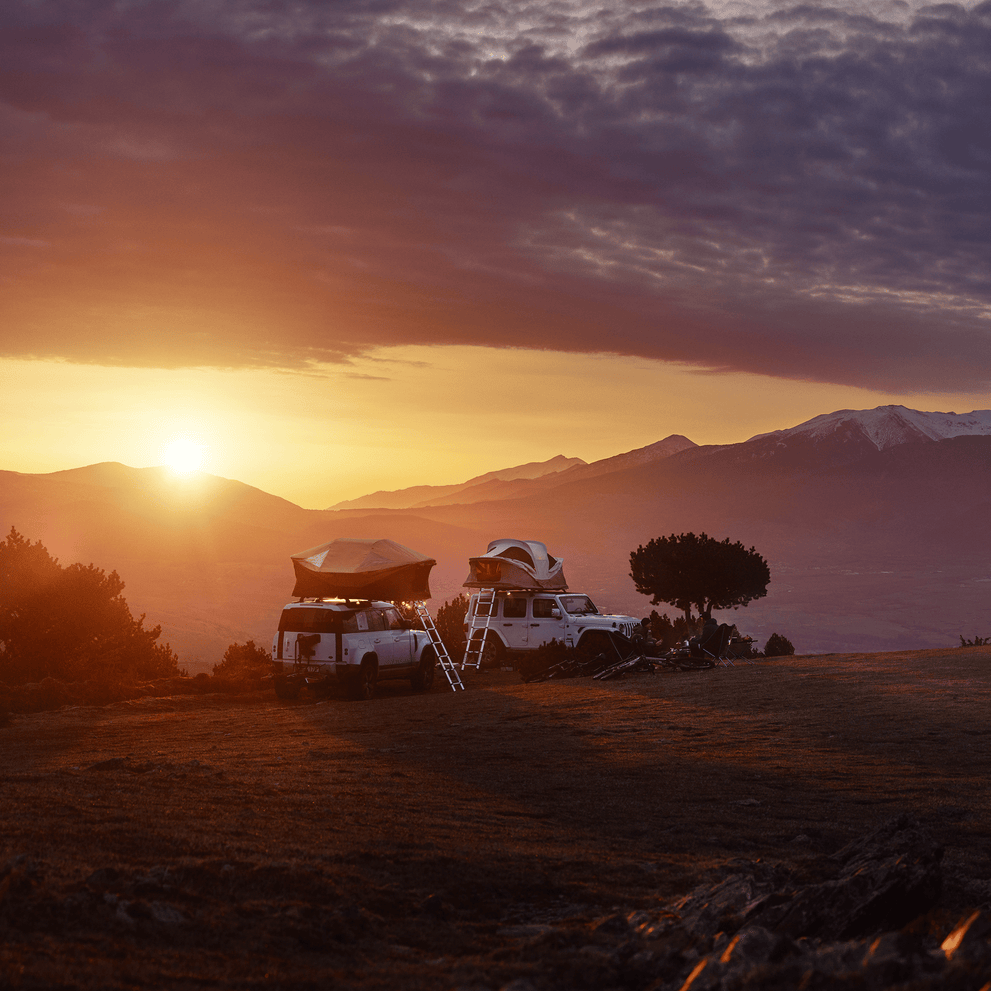 Two cars with roof top tents parked in a hilly terrain in sunset