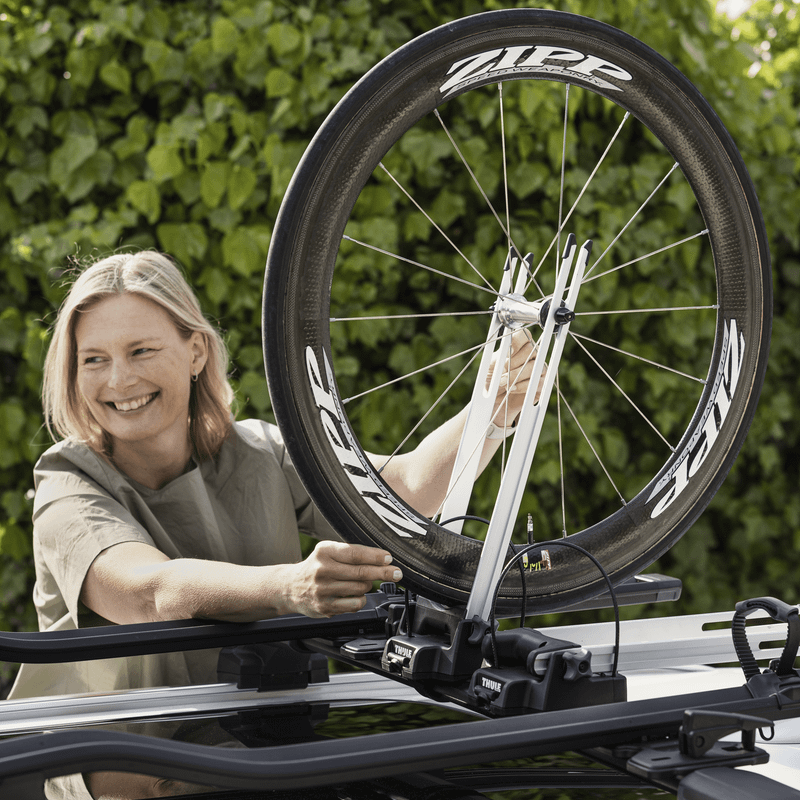 A woman is mounting a bike wheel to her car using a Thule Front Wheel Holder.