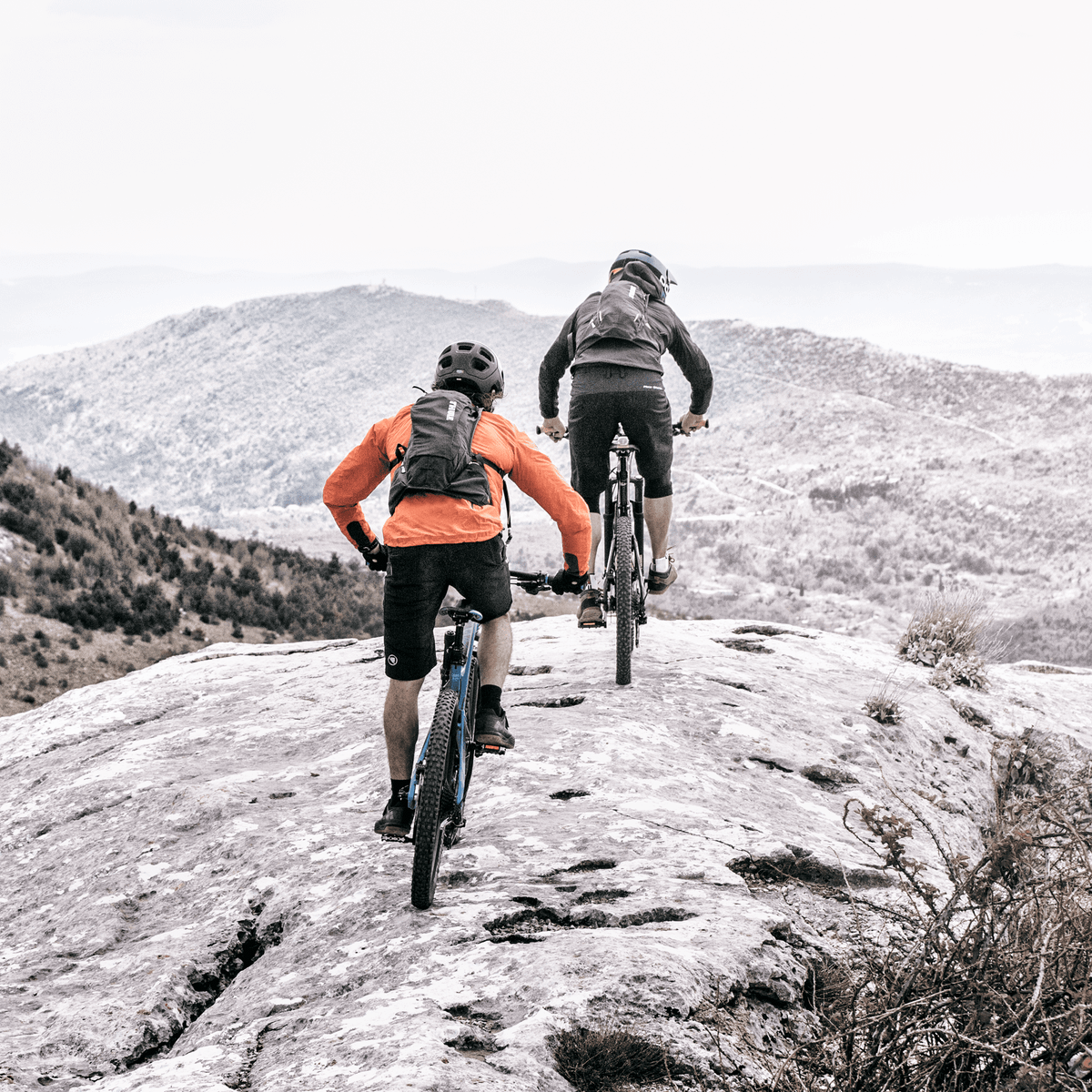 Two people go mountain biking in a rocky trail with a Thule Vital hydration backpack.