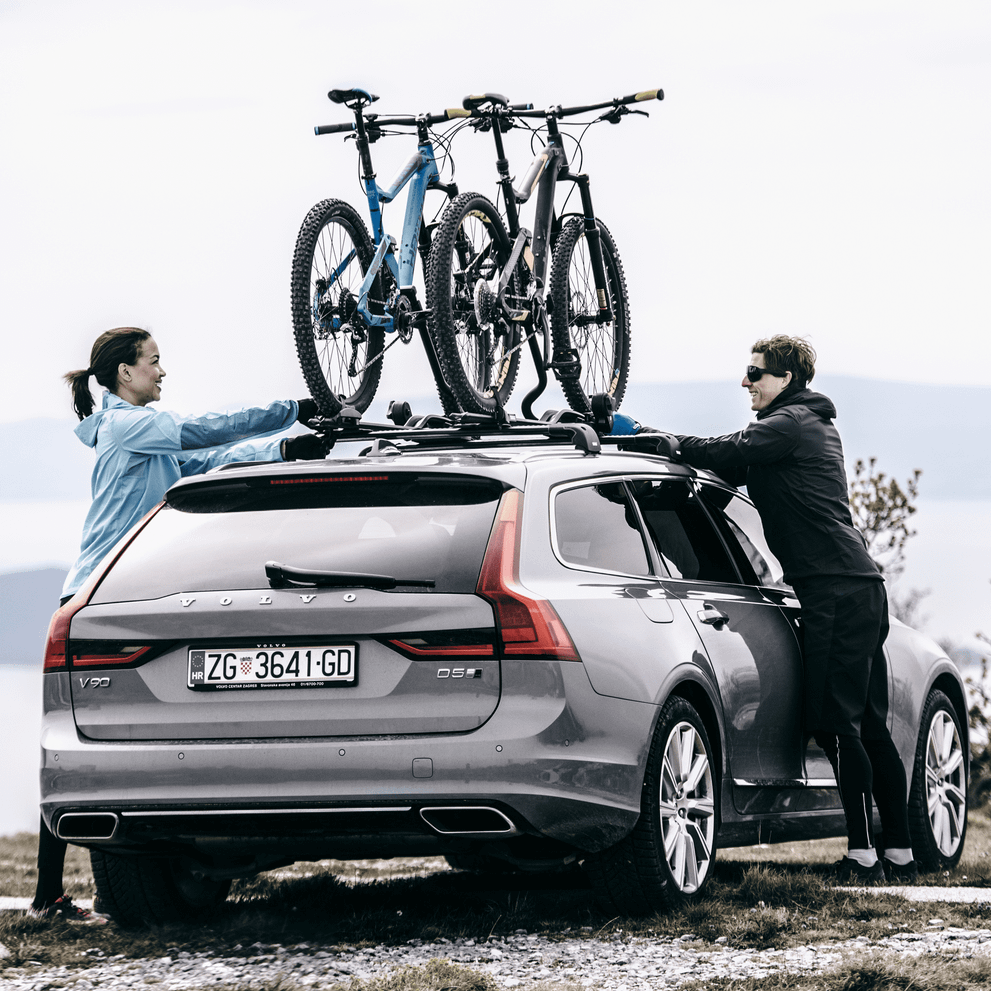 Two people install their bikes into a Thule ProRide roof bike rack.