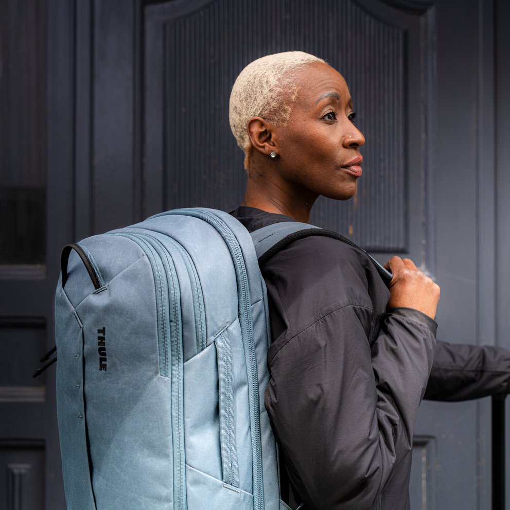A woman with blonde hair is carrying the blue Thule Aion backpack.