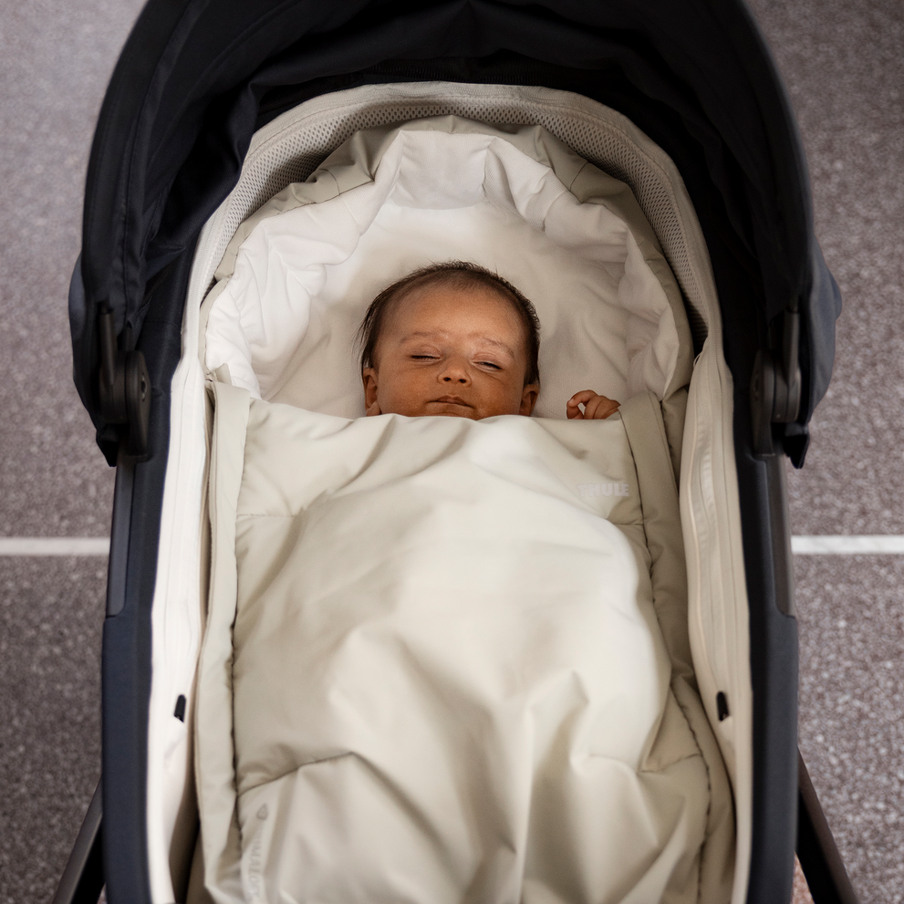 Baby lying in a stroller, securely wrapped in the Thule Elements high-performance footmuff for warmth and protection.
