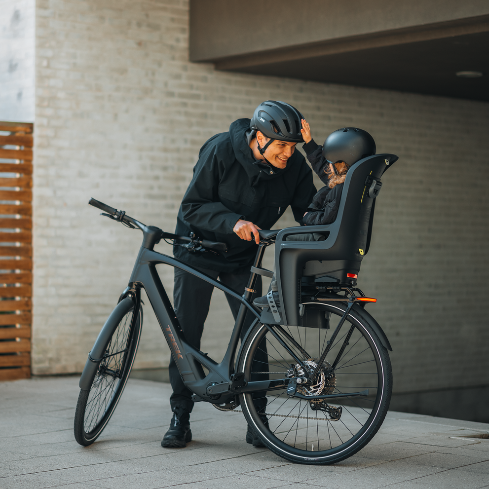Padre asegurando a un niño en el asiento trasero para bicicleta Thule RideAlong 2 antes de un paseo.