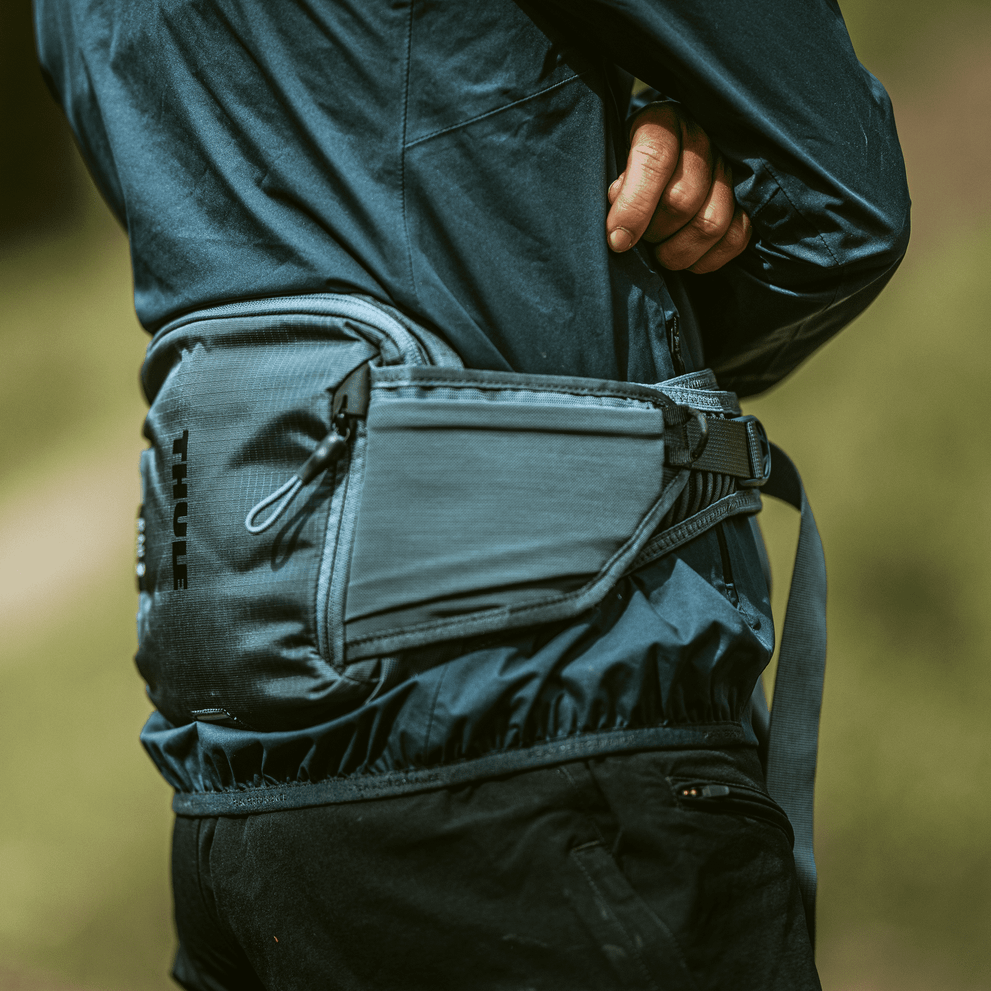 A person with arms folded is carrying a Thule Rail 0L hydration Hip Pack.