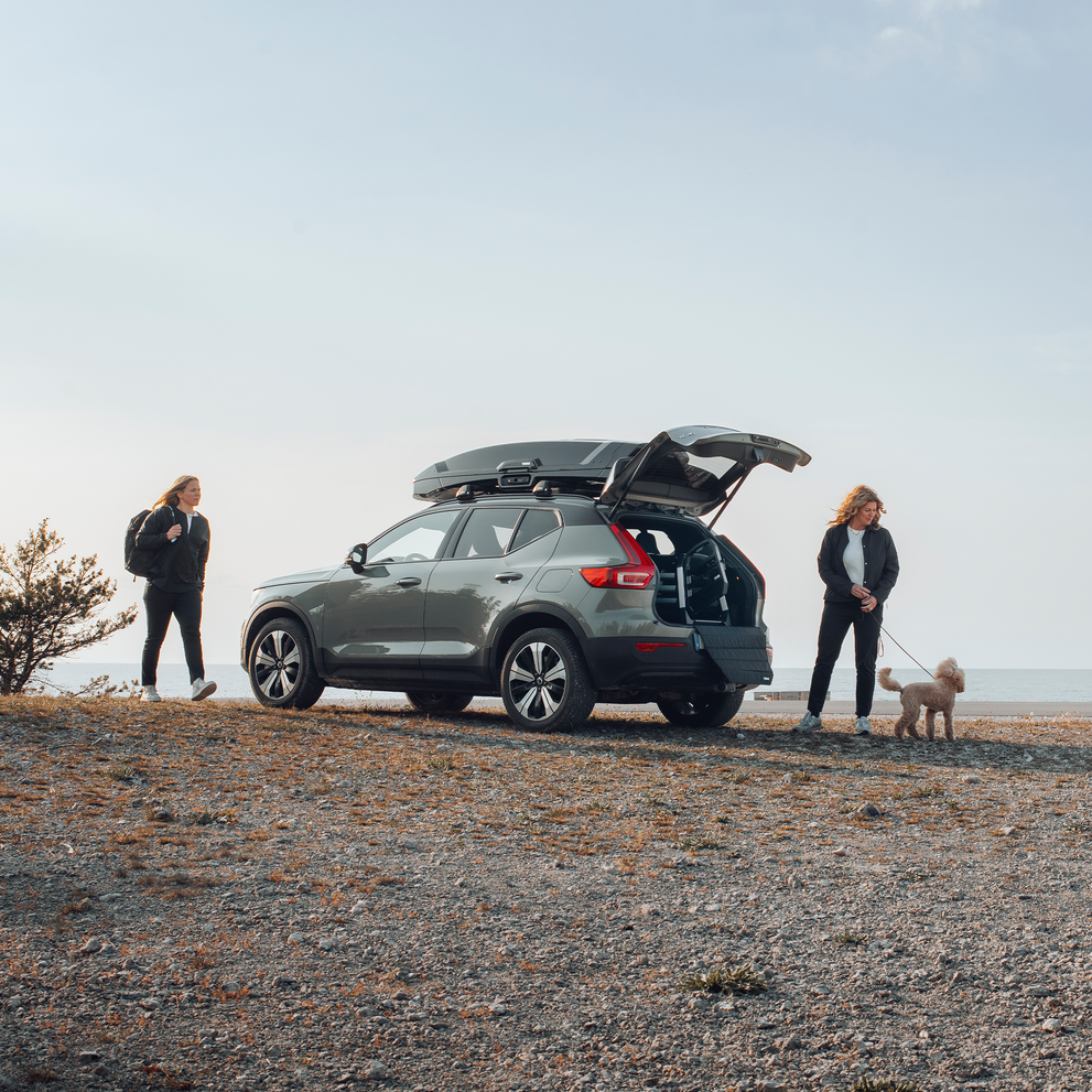 Two women stand with their dog next to a car with the trunk open and a car dog crate inside.